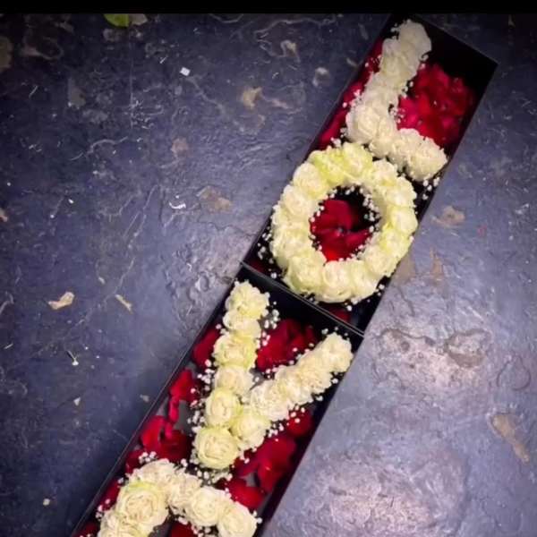 Long box of cream roses arranged as letters over red petals
