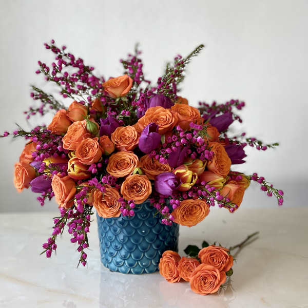 Orange and purple bouquet in a blue textured vase with a few roses beside it