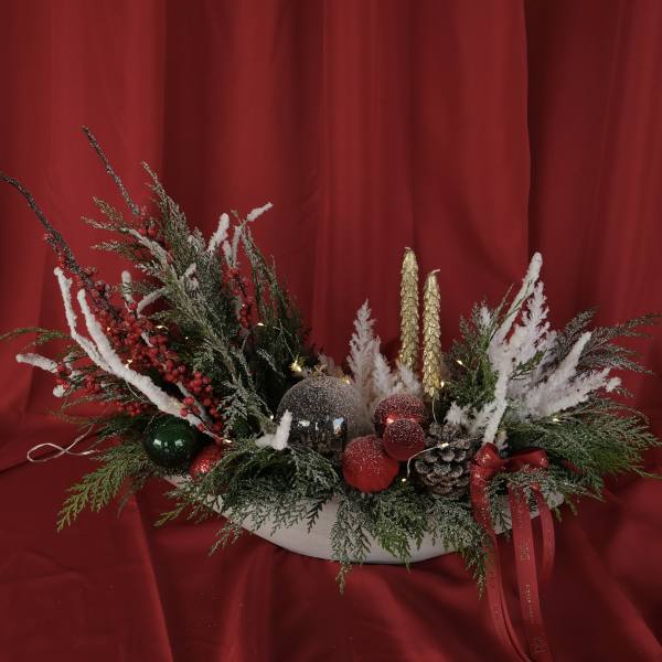 Holiday centerpiece with frosted evergreens, red berries, and ornaments in a white bowl