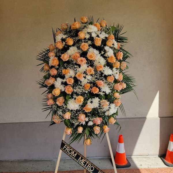 Tall standing spray of peach roses and white flowers on an easel.