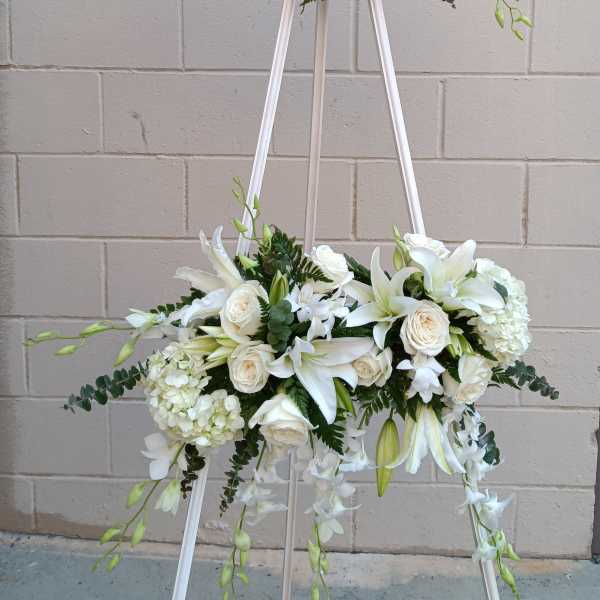 White floral arrangement on a standing easel with roses and lilies