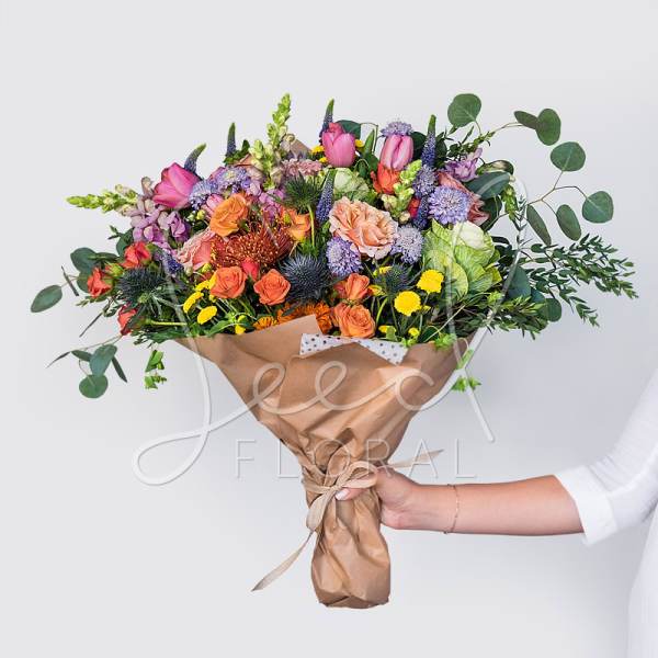 Large hand-tied bouquet of bright mixed flowers wrapped in brown paper