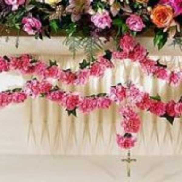 Pink floral cross arrangement on a white draped stand