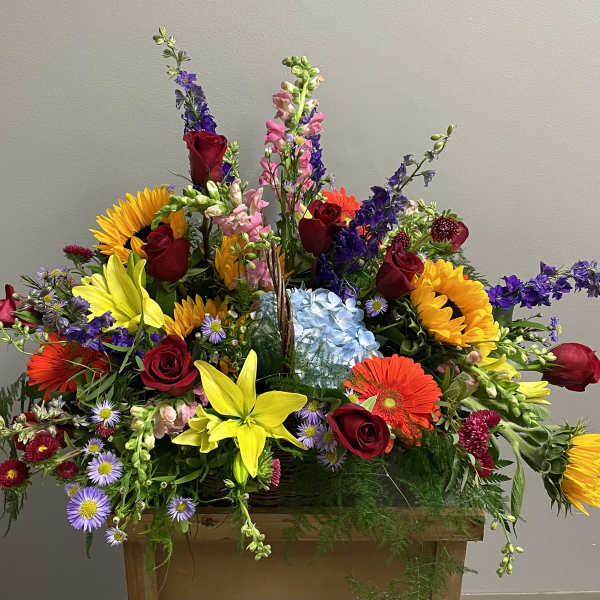 Large mixed flower arrangement with sunflowers, roses, and lilies in a wooden container