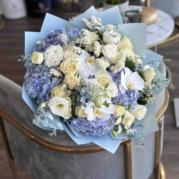 Bouquet of blue hydrangeas, white roses, and white orchids wrapped in pale blue paper