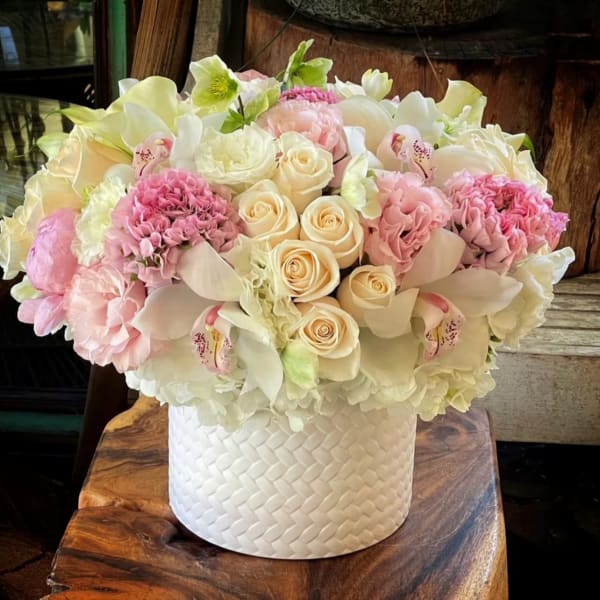 Low round arrangement of white and blush flowers in a white textured cylinder container