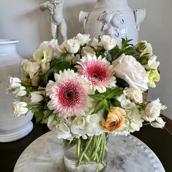 Bouquet of pink gerbera daisies, white roses, and pale hydrangeas in a glass vase