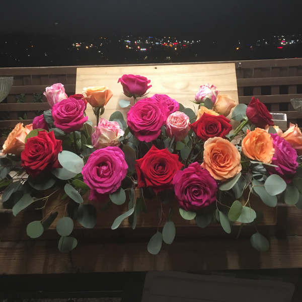 Arrangement of multicolored roses with eucalyptus on a wooden ledge
