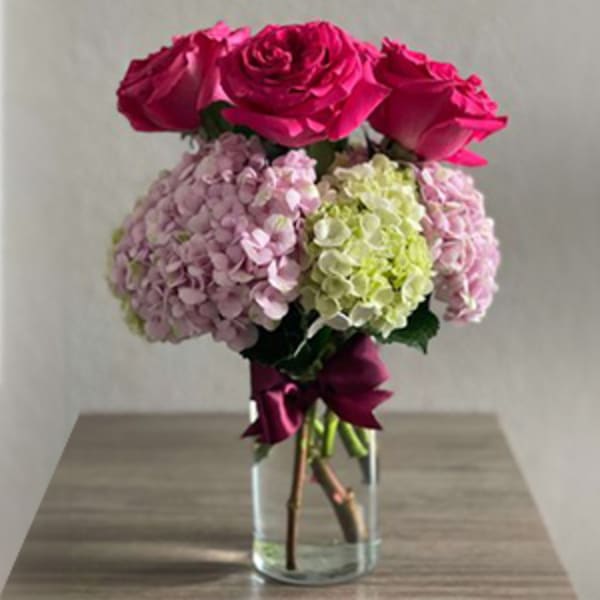 Pink roses and hydrangeas in a clear glass vase with a ribbon