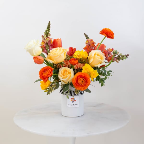 Bright mixed bouquet in a white vase with orange, yellow, and cream flowers