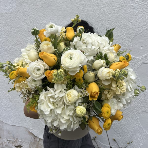 Large bouquet of white and yellow flowers held in front of a wall