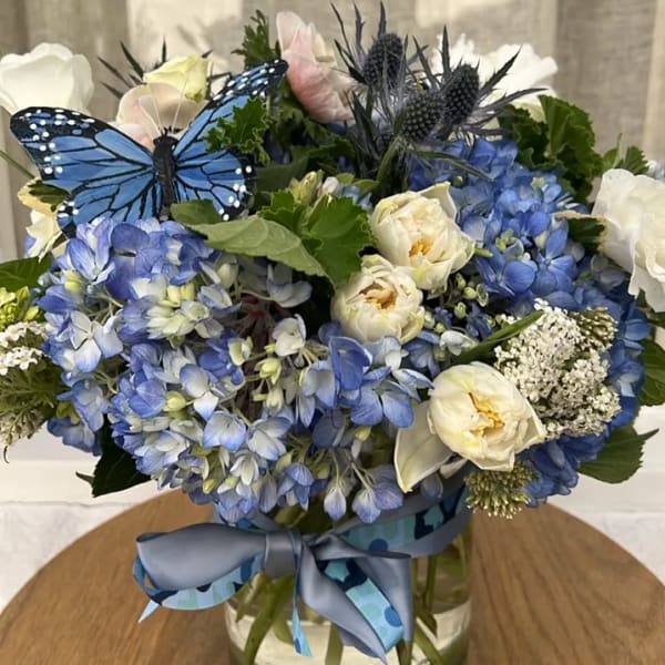Blue and white flower arrangement in a glass vase with a ribbon and butterfly decoration