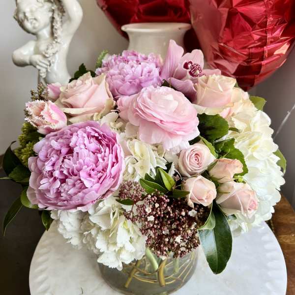 Pink and white flower arrangement in a glass vase with red heart balloons