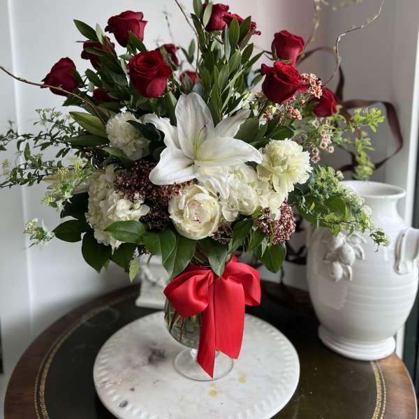 Red roses and white lilies arranged in a glass vase with a red ribbon