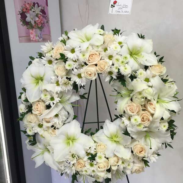 White floral wreath on a stand with cream roses and lilies