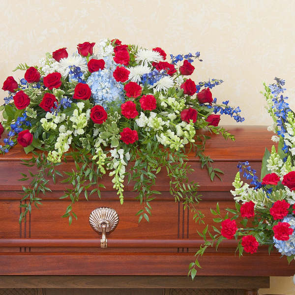 Red, white, and blue funeral flowers arranged around a wooden casket.