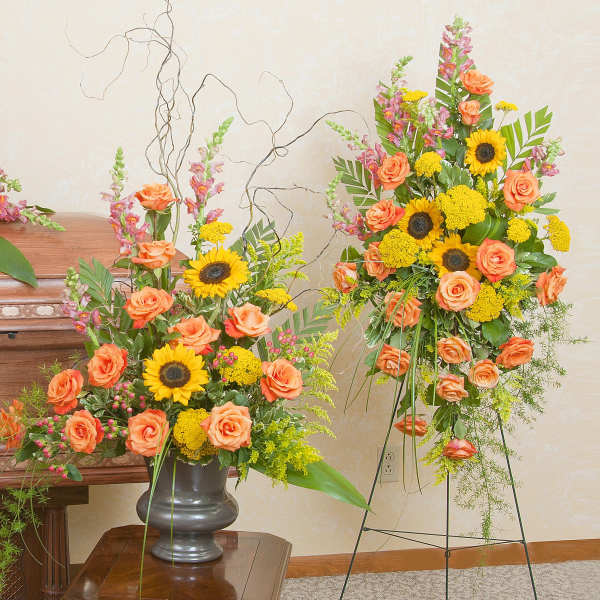 Three floral funeral arrangements with orange roses and sunflowers around a casket.