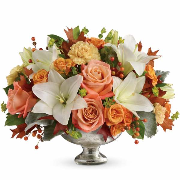 Orange roses and white lilies arranged in a silver pedestal vase