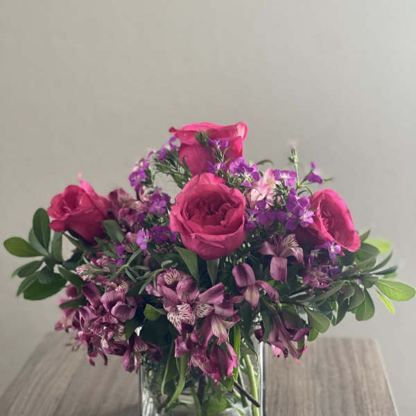 Pink roses and purple flowers arranged in a clear glass vase.