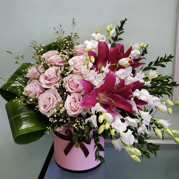 Pink roses and magenta lilies arranged in a pink hatbox