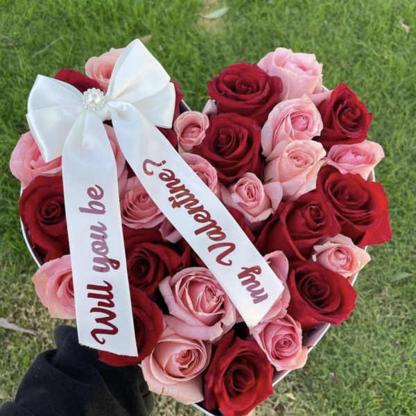 Heart-shaped bouquet of red and pink roses with white ribbons