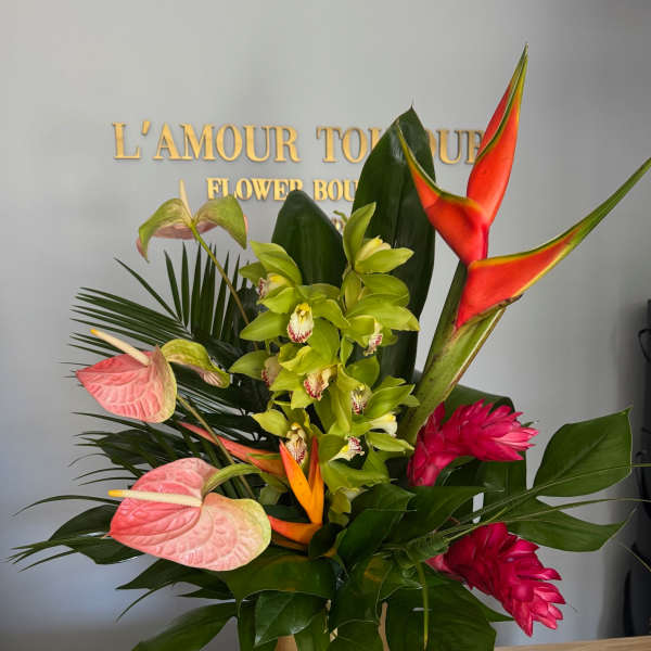 Tropical arrangement with green orchids, pink blooms, and orange heliconia in a gold pedestal vase