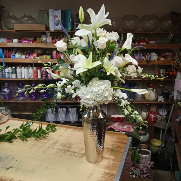 White lilies and roses arranged in a tall silver vase