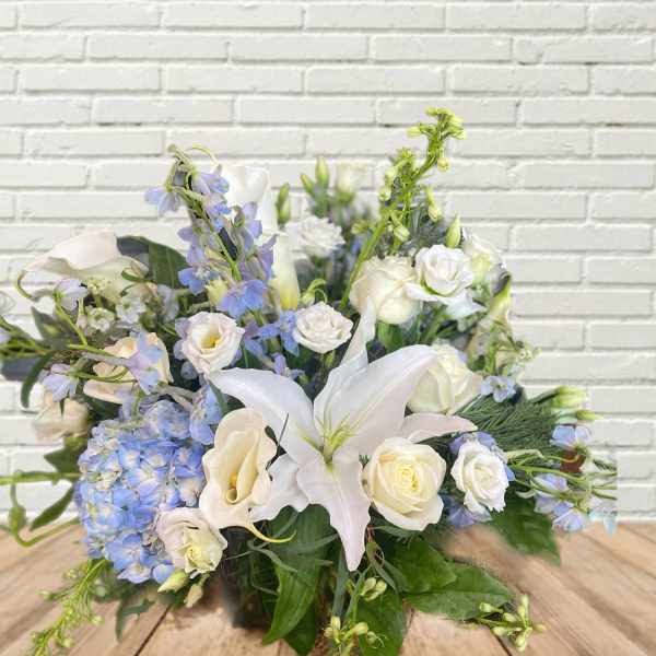 White lilies, calla lilies, roses, and blue flowers in a low arrangement