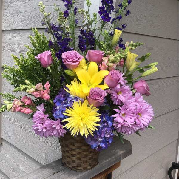 Mixed bouquet in a woven basket with pink, yellow, purple, and blue flowers