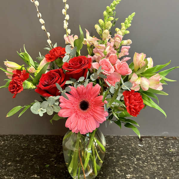 Mixed bouquet with red roses, pink gerbera daisy, and pink lilies in a glass vase