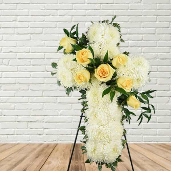 White floral cross with yellow roses on a stand
