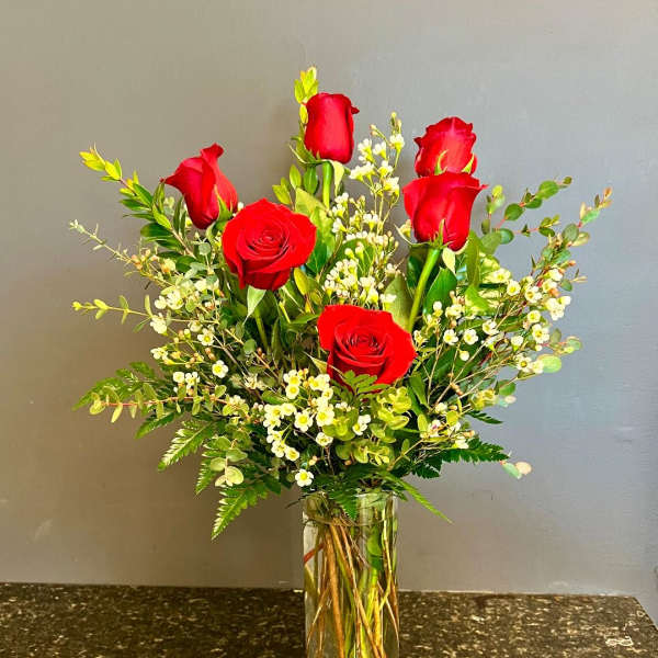 Red roses arranged in a clear glass vase with small white filler flowers