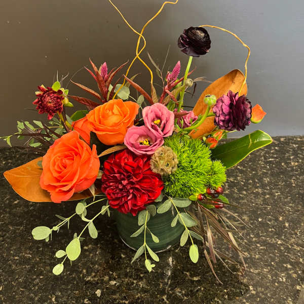Mixed floral arrangement with orange roses, pink blooms, and red flowers in a green vase
