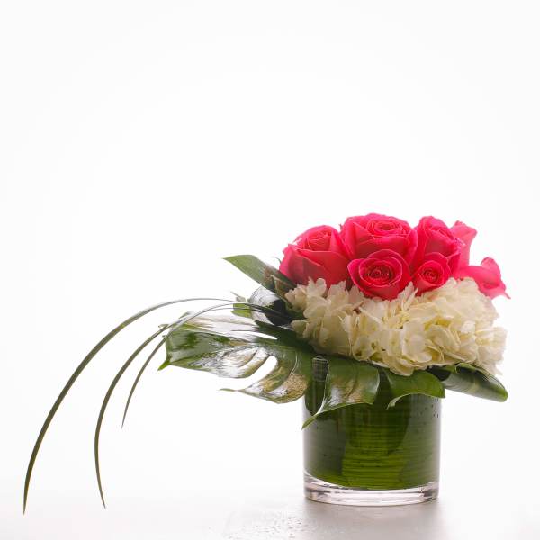 Pink roses and white hydrangeas in a glass vase with broad leaves