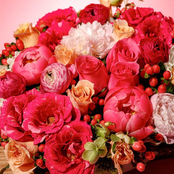 Pink and peach bouquet with roses and peonies on a wooden surface