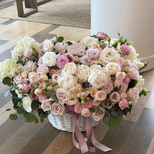 Large pastel flower arrangement in a white basket with pink ribbon