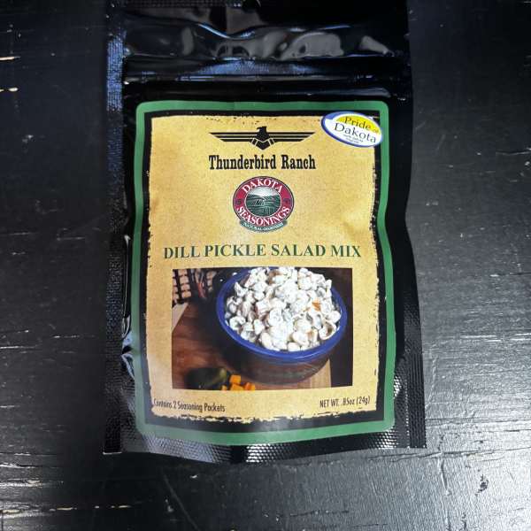A packet of dill pickle salad mix on a dark surface.