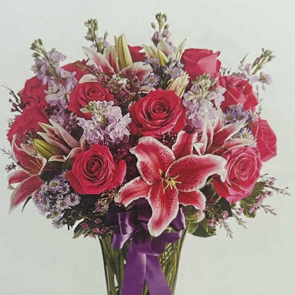 Bouquet of red roses and pink lilies in a clear glass vase with a purple ribbon
