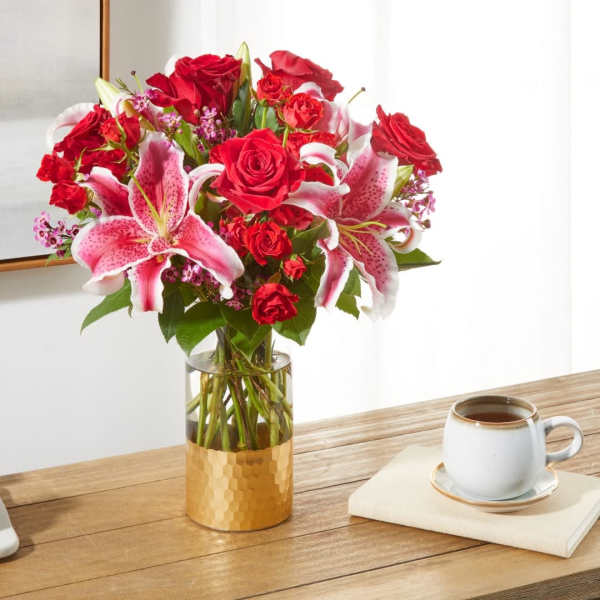 Red roses and pink lilies in a gold vase on a table