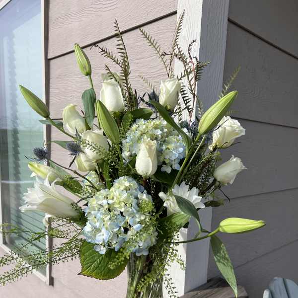 White roses and lilies arranged with blue hydrangeas in a glass vase