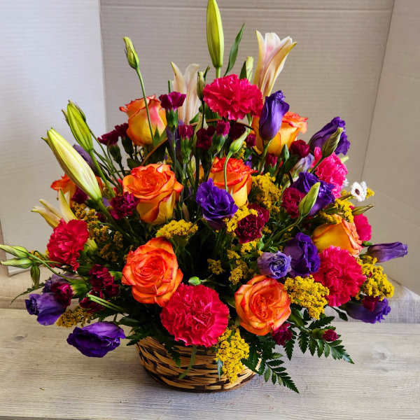Basket arrangement of orange roses, purple lisianthus, and pink carnations
