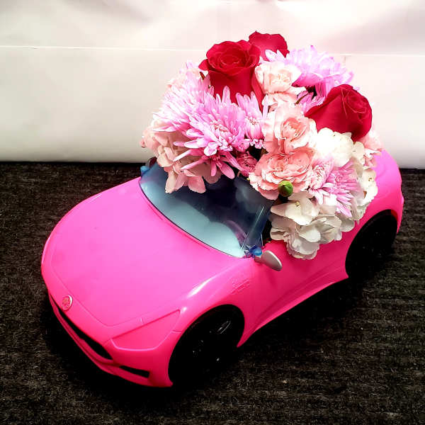Pink toy car topped with a bouquet of red, pink, and white flowers