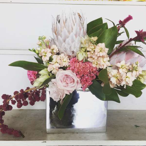 Pink and cream floral arrangement in a mirrored square vase