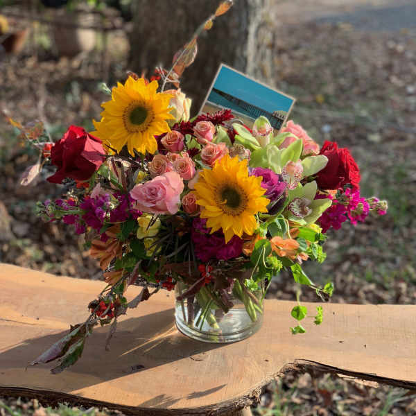 Mixed bouquet with sunflowers, roses, and orchids in a glass vase