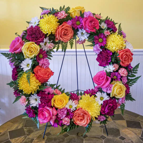 Large floral wreath on a stand with pink, yellow, white, and coral blooms