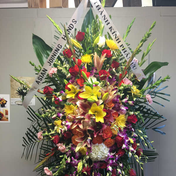 Large standing floral spray with mixed blooms and white condolence ribbons