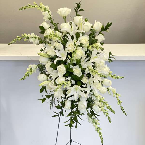 Tall white floral standing arrangement with roses and lilies on a metal easel