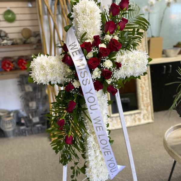 Standing floral cross with red roses and white chrysanthemums, with a memorial ribbon.