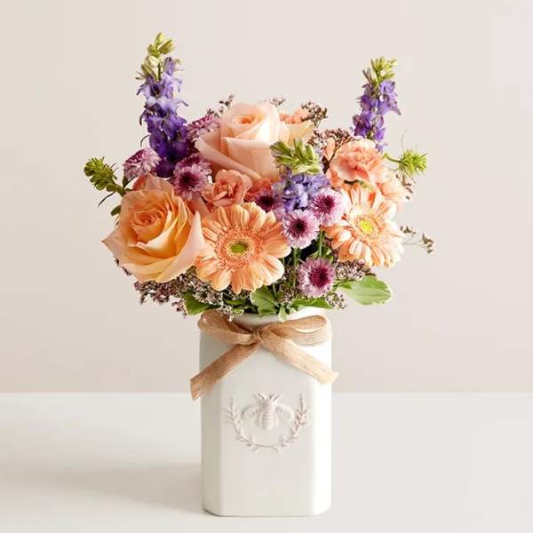 Peach and lavender flower bouquet in a white vase with a ribbon