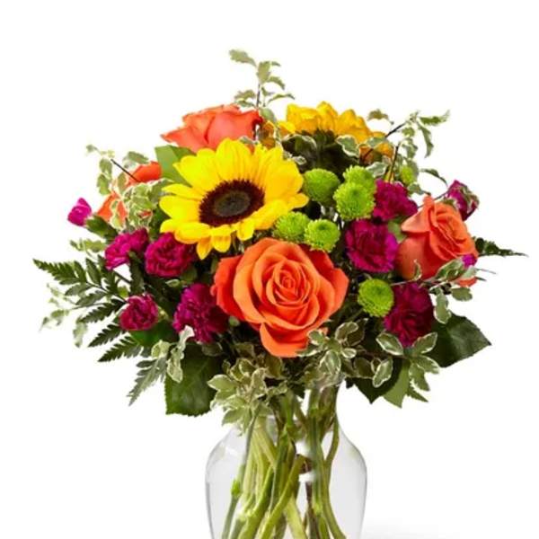 Bouquet of orange roses, yellow sunflowers, and magenta flowers in a glass vase